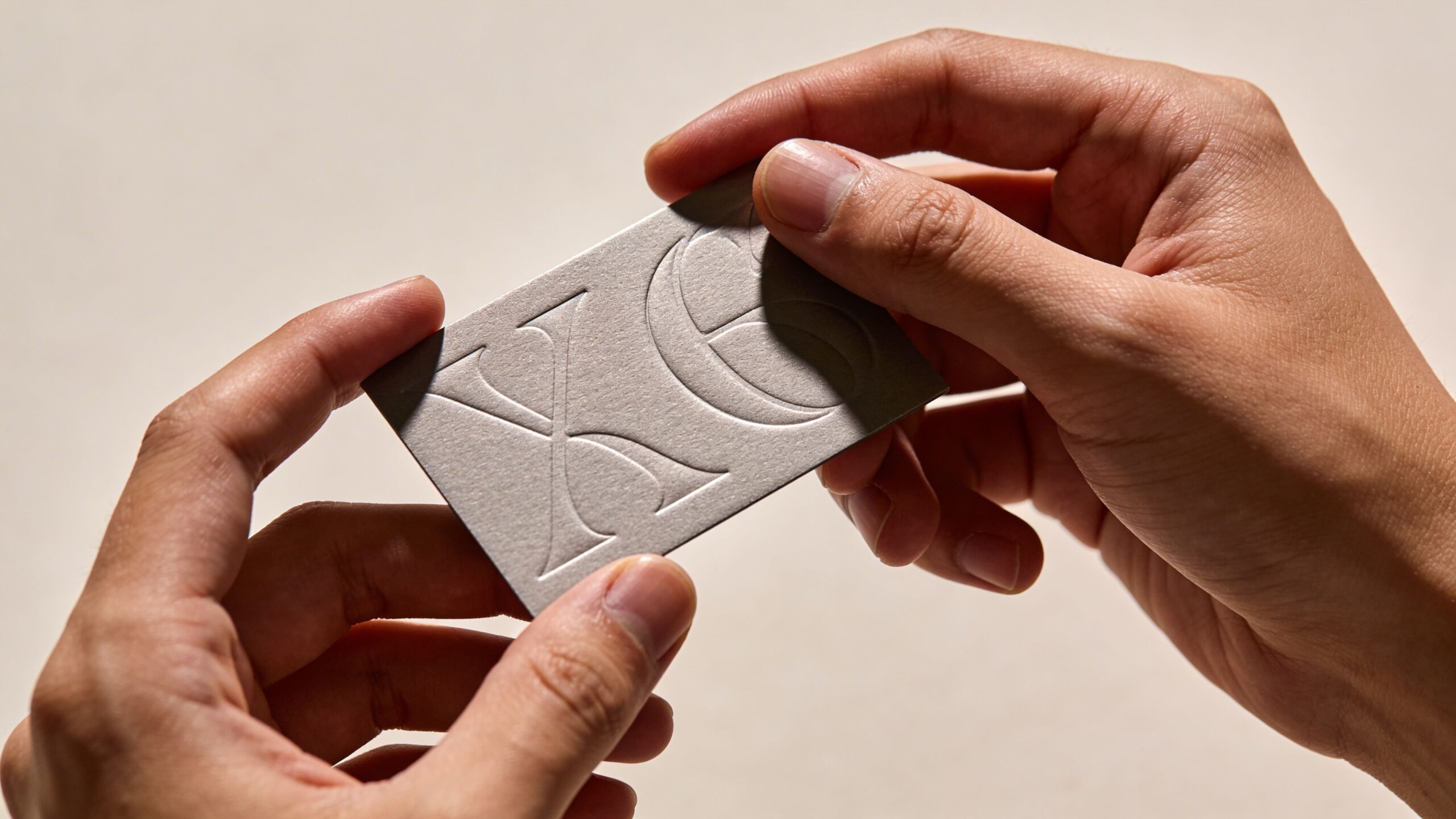 Eine Hand hält eine kleine, graue Karte mit dem eingeprägten Logo XE auf einem beigefarbenen Hintergrund.